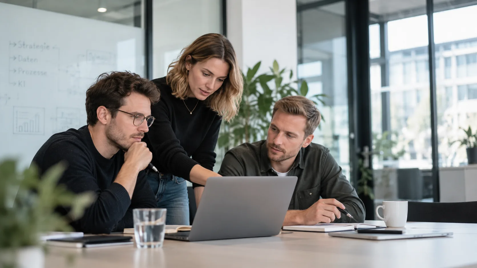 Drei Personen besprechen gemeinsam etwas an einem Laptop in einem hellen Büro.
